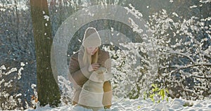 A young woman petting her dog while walking together in a picturesque winter park