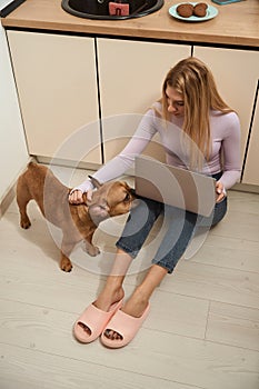 Young woman petting her French bulldog in kitchen