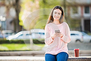 Young woman with phone browse in internet and drink coffee in the city street