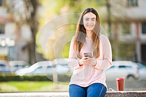 Young woman with phone browse in internet and drink coffee in the city street