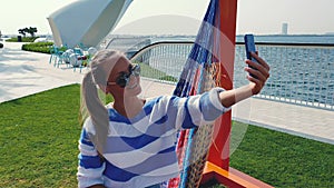 Young woman with phone in the hammock at the city background.