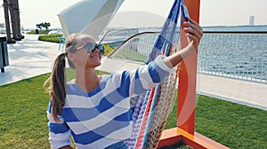 Young woman with phone in the hammock at the city background.