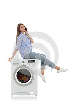 Young woman with phone sitting on washing machine