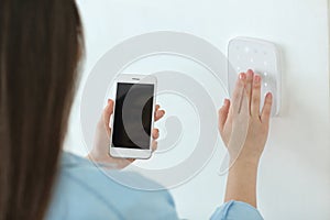 Young woman with phone using security system indoors