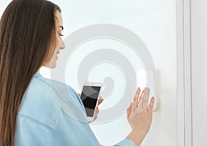 Young woman with phone using security system indoors