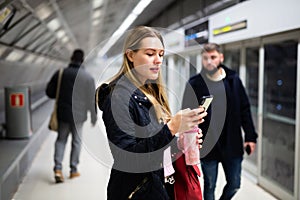 Young woman with phone waiting at subway station