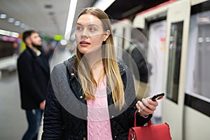 Young woman with phone waiting at subway station