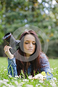 Young woman photographer with camera lie down on grass