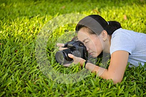 Young woman photographer with camera lie down on grass with copy space