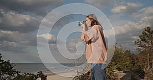 Young woman photographer takes pictures of the sea using digital camera