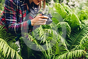 Young woman photographer taking photos on digital camera in summer park. Happy freelancer taking pictures of fern