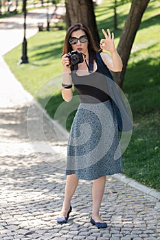 Young woman photographer, tourist holds a camera and shows the