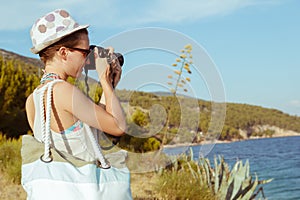 Young woman photographer, tourist using digital camera taking photo by the sea