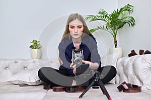 Young woman photographer with vintage camera recording video on smartphone