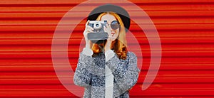 Young woman photographer with vintage film camera wearing a black round hat over red