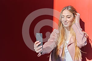 Young woman photographing herself with a mobile on a red background