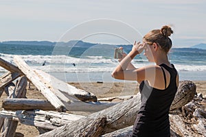Young woman photographing ocean with cellphone