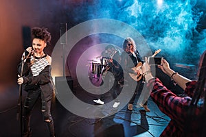 Young woman photographing rock and roll band performing hard rock music