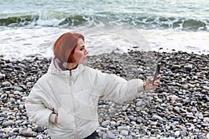 Young woman photographs herself on the phone on seacoast against the backdrop of the sea waves