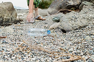 Young woman picking up the plastic bottle garbage, cleaning on the coastal strip.