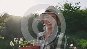 A young woman picks up a pot of plants and smiles. Real time. Jib shot. Earth Day Concept
