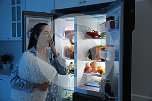 Young woman with pillow near open refrigerator