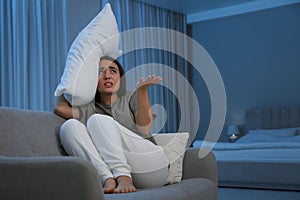 Young woman with pillow suffering from noisy neighbours in living room at night