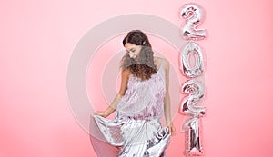 Young woman on a pink background with silver balls in the form of the numbers 2021 photo