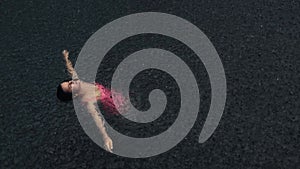 Young woman in pink bikini floating on the back in the dark water of simming pool, ocean or lake under the rain drops