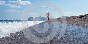 Young woman in pink bikini running on a beautiful pebble beach