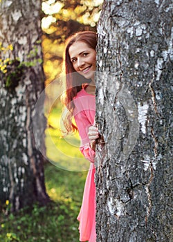 Young woman in pink dress, peek a boo behind the tree, with suns