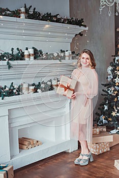 A young woman in a pink dress standing by the fireplace on the background of a Christmas tree