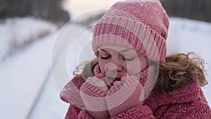 Young woman in pink faux fur coat blows snow from palms in winter