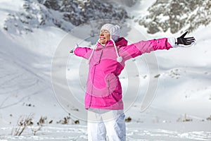 Young woman in pink ski jacket, gloves and pants, arms spread, e