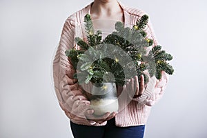 Young woman in a pink sweater holds a Christmas tree in her hands