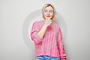 Young woman in pink sweater pondering over gray background