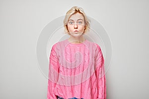 Young woman in pink sweater pouting against a gray background