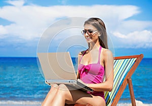 A young woman in a pink swimsuit with a computer on the beach