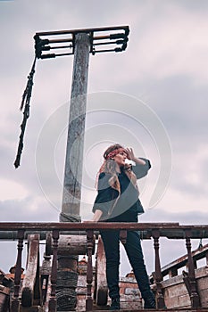 Young woman pirate in vintage clothes on an old wooden ship looks into the distance in search of land