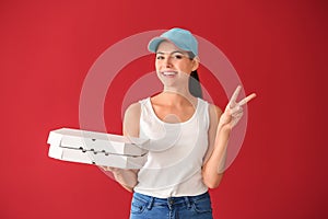 Young woman with pizza boxes showing victory sign on color background. Food delivery service