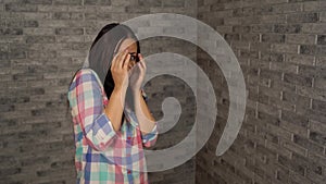 A young woman in a plaid shirt shows a fright on a brick background. A woman was gripped by fear.