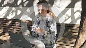 Young woman in plaid shirt spending lunch break in cafe surfing internet on smartphone