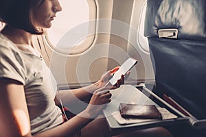 Young woman on a plane with a smartphone in her hands