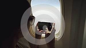 Young woman in plane taking photo on her smartphone during flight