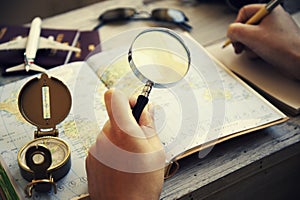 Young woman planning her vacation with travel map. She`s looking for next destination with magnifying glass in her hand.