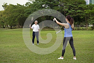 young woman playing badminton with senior man in the park