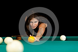 Young woman playing billiard. Black background.