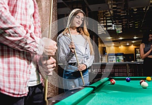 Young woman playing in billiard. Posing near the table with a cue in her hands