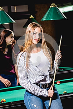 Young woman playing in billiard. Posing near the table with a cue in her hands