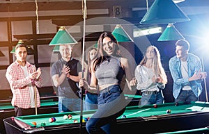 Young woman playing in billiard. Posing near the table with a cue in her hands